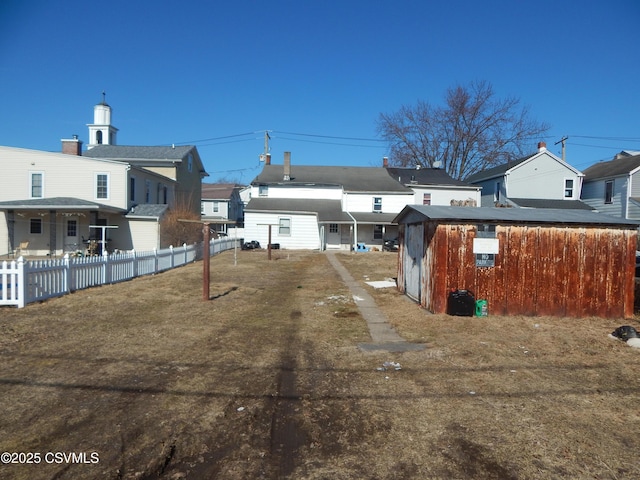 rear view of property with an outdoor structure, fence, and a residential view