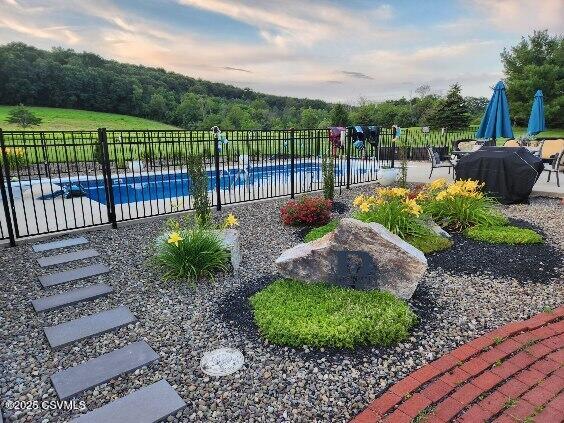 pool at dusk with a patio area, a grill, fence, and a fenced in pool