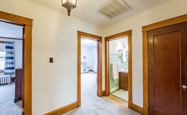 hallway with carpet floors, radiator heating unit, visible vents, and baseboards