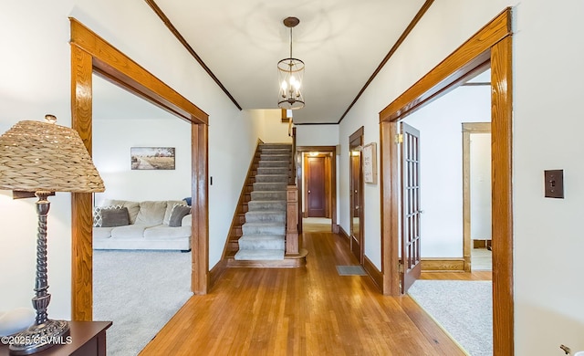 hall with a notable chandelier, crown molding, visible vents, stairway, and wood finished floors