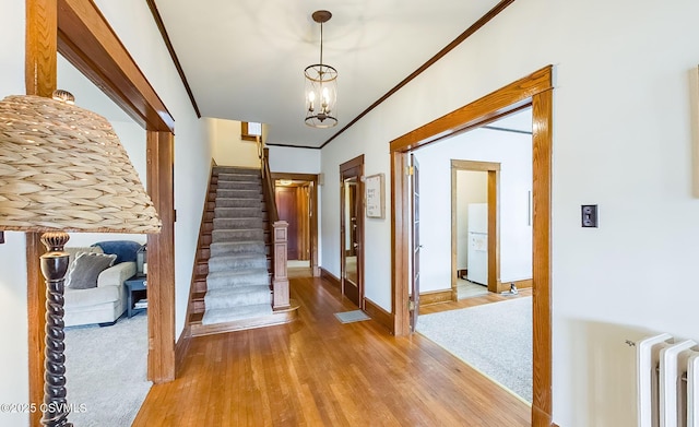 foyer featuring wood finished floors, baseboards, ornamental molding, stairway, and radiator heating unit