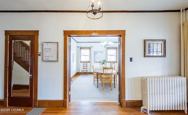 unfurnished dining area featuring wood finished floors, baseboards, stairs, radiator, and an inviting chandelier