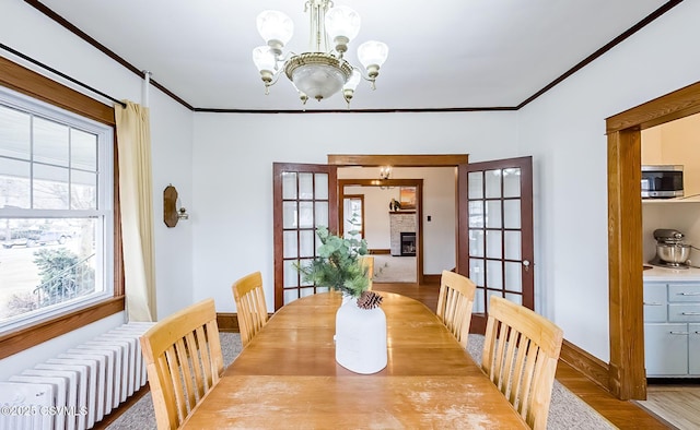 dining space with radiator heating unit, ornamental molding, wood finished floors, an inviting chandelier, and a stone fireplace