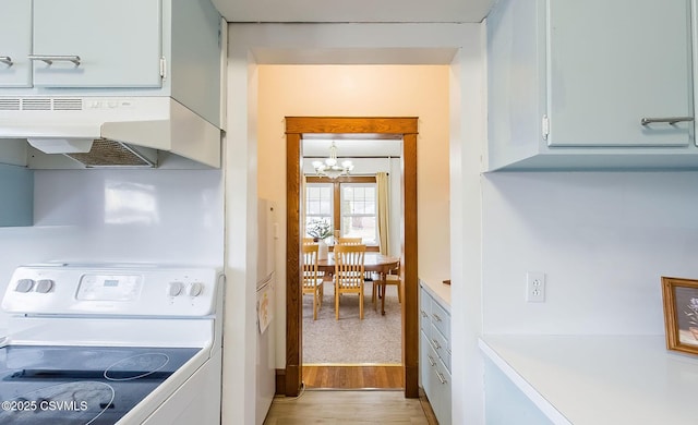 kitchen with a chandelier, light wood-style flooring, under cabinet range hood, electric stove, and light countertops