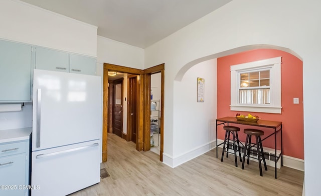 kitchen with light wood-type flooring, freestanding refrigerator, arched walkways, and baseboards