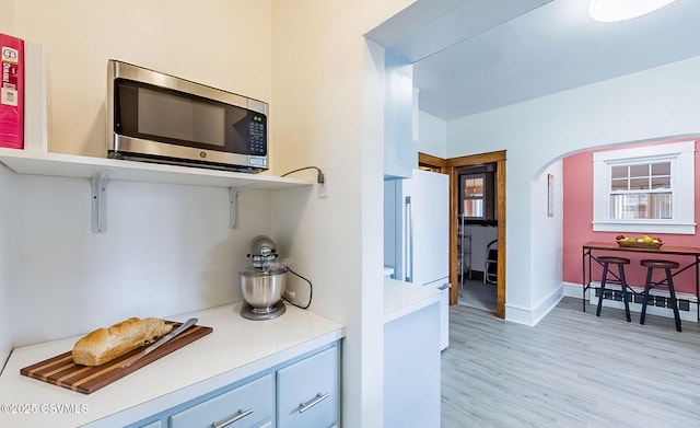 bar with baseboards, arched walkways, stainless steel microwave, freestanding refrigerator, and light wood-style floors