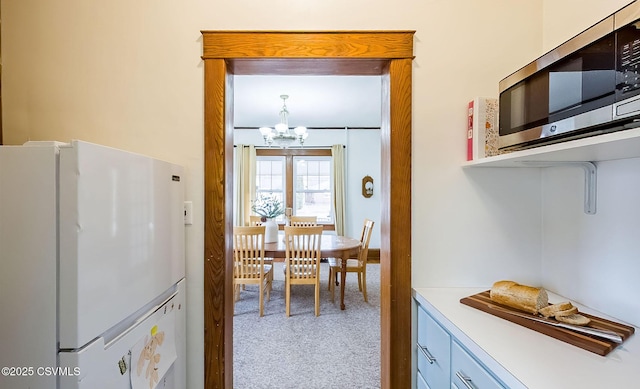 kitchen featuring a notable chandelier, light countertops, stainless steel microwave, freestanding refrigerator, and carpet flooring