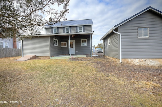 rear view of property featuring a chimney, fence, metal roof, and a lawn