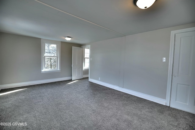 spare room featuring dark colored carpet and baseboards