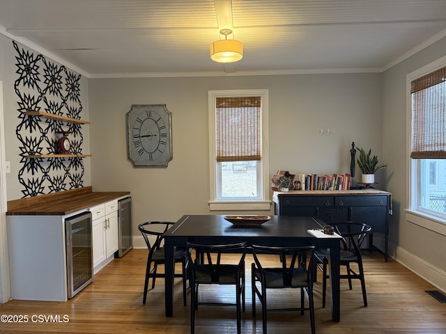 dining space with beverage cooler, light wood finished floors, and crown molding