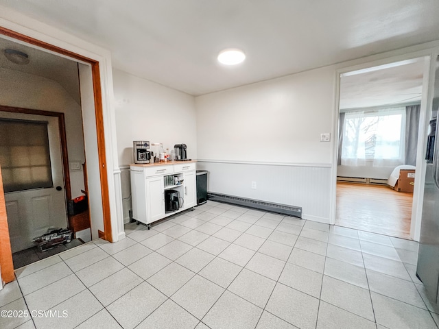 kitchen featuring white cabinets, light tile patterned floors, baseboard heating, and wainscoting