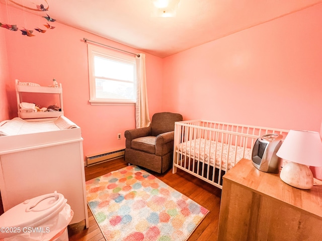 bedroom featuring a crib, baseboard heating, and wood finished floors