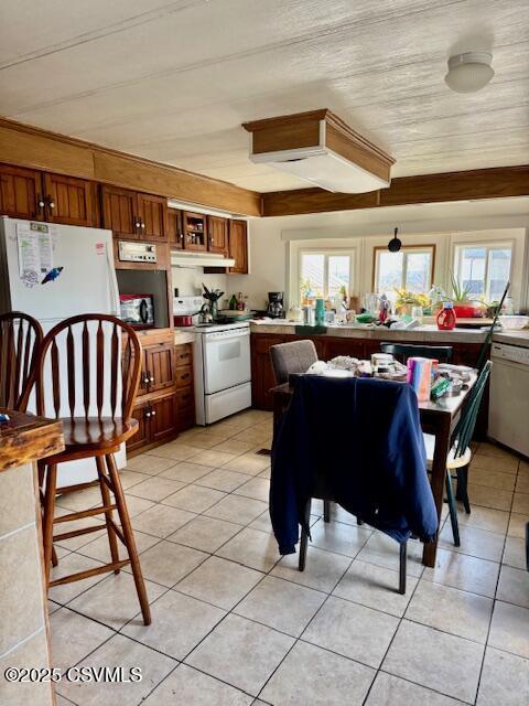 kitchen with light tile patterned floors, white appliances, a wealth of natural light, and brown cabinets