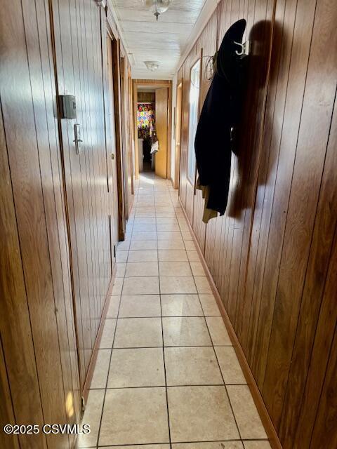 hall featuring light tile patterned floors and wooden walls