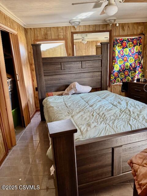 bedroom featuring ornamental molding, tile patterned floors, a ceiling fan, and wooden walls