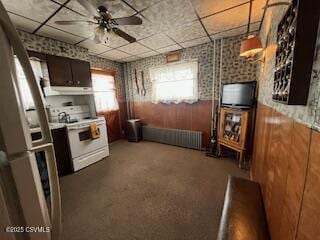 kitchen with electric stove, a wainscoted wall, a ceiling fan, wood walls, and a drop ceiling