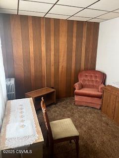 sitting room with carpet floors, radiator heating unit, a drop ceiling, and wooden walls