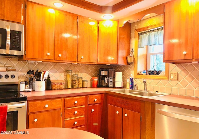 kitchen with brown cabinets, stainless steel appliances, tasteful backsplash, light countertops, and a sink