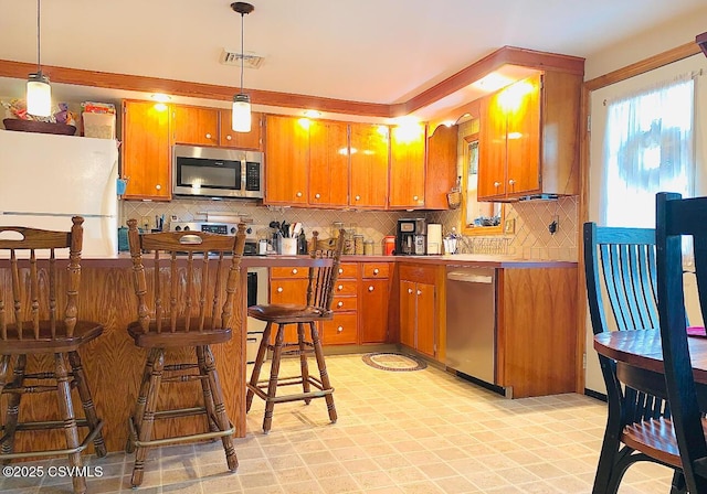 kitchen featuring visible vents, appliances with stainless steel finishes, backsplash, brown cabinets, and pendant lighting