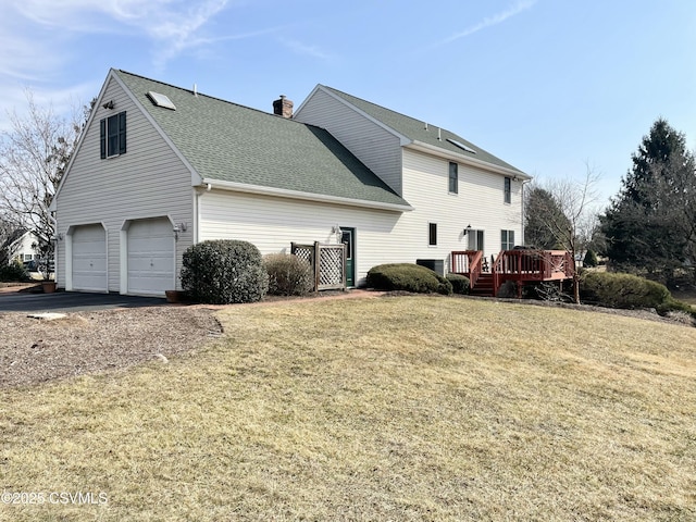 view of side of home featuring roof with shingles, a chimney, a lawn, an attached garage, and a deck