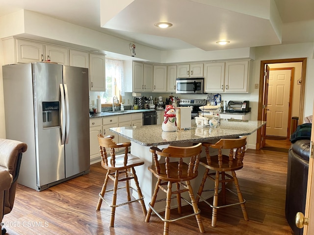 kitchen featuring appliances with stainless steel finishes, a sink, dark wood finished floors, and a breakfast bar area