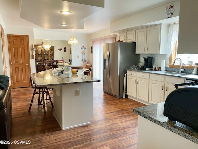 kitchen featuring dark wood finished floors, a breakfast bar area, a sink, dark stone counters, and stainless steel fridge with ice dispenser