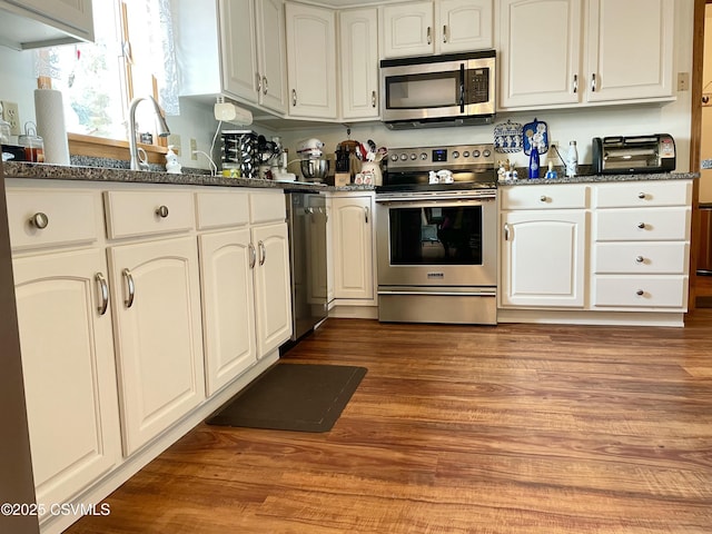 kitchen featuring white cabinets, dark stone countertops, stainless steel appliances, and wood finished floors