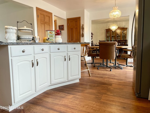 kitchen featuring an inviting chandelier, freestanding refrigerator, white cabinetry, dark stone countertops, and wood finished floors