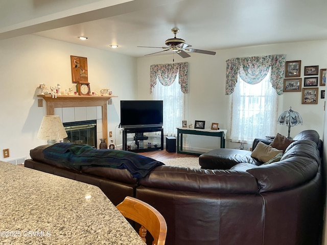 living area with a tile fireplace, a healthy amount of sunlight, visible vents, and wood finished floors