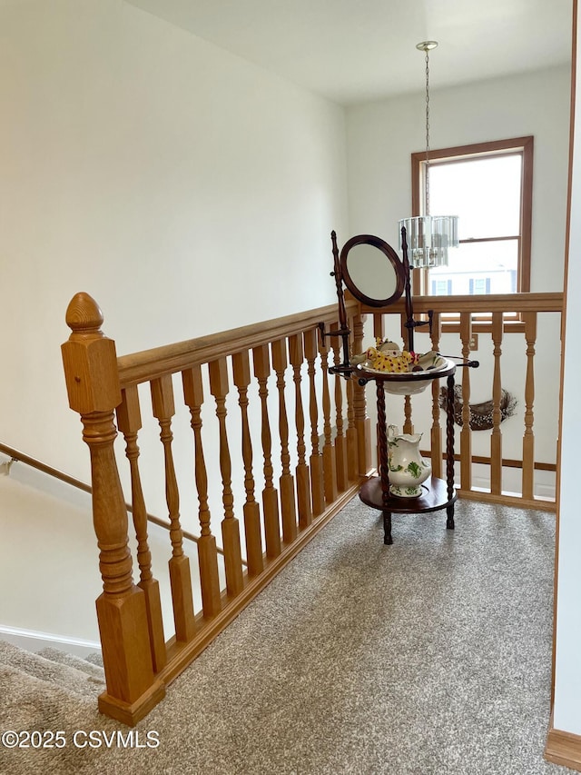 interior space featuring carpet, baseboards, a notable chandelier, and an upstairs landing