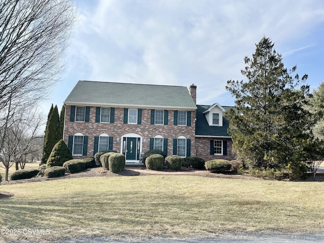 colonial inspired home featuring a front lawn, a chimney, and brick siding