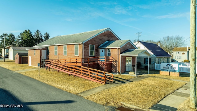 view of front of house featuring brick siding, an outdoor structure, a deck, and fence