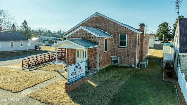 view of home's exterior with brick siding, central AC unit, a lawn, and fence