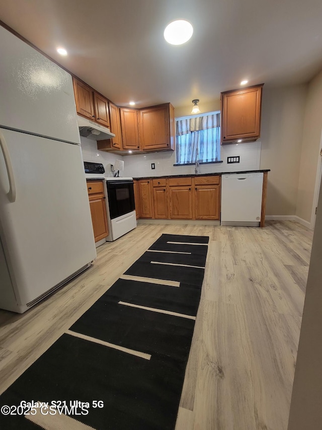 kitchen featuring brown cabinets, light wood-style flooring, under cabinet range hood, a sink, and white appliances