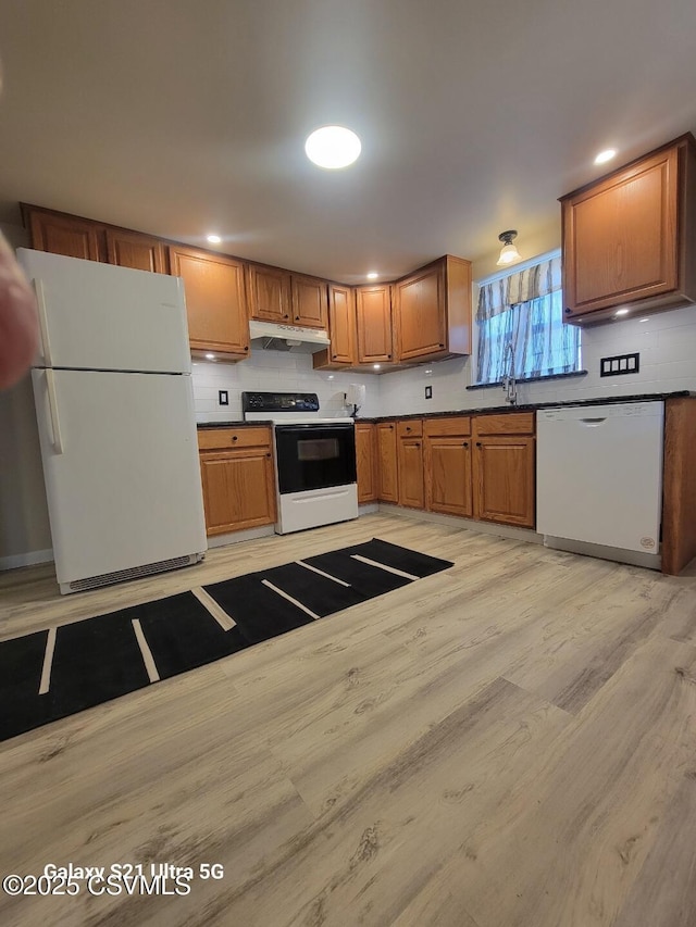 kitchen with under cabinet range hood, a sink, white appliances, light wood-style floors, and brown cabinetry