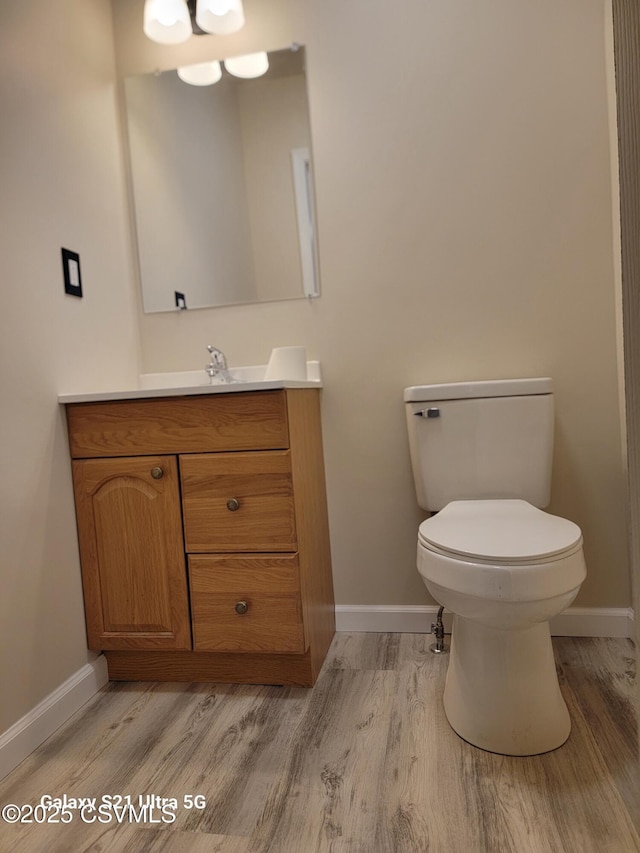 half bathroom with baseboards, toilet, and wood finished floors