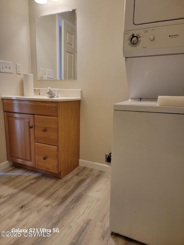 bathroom with vanity, wood finished floors, stacked washer and clothes dryer, and baseboards