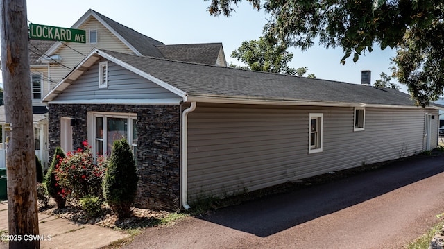 view of side of property with stone siding and a shingled roof