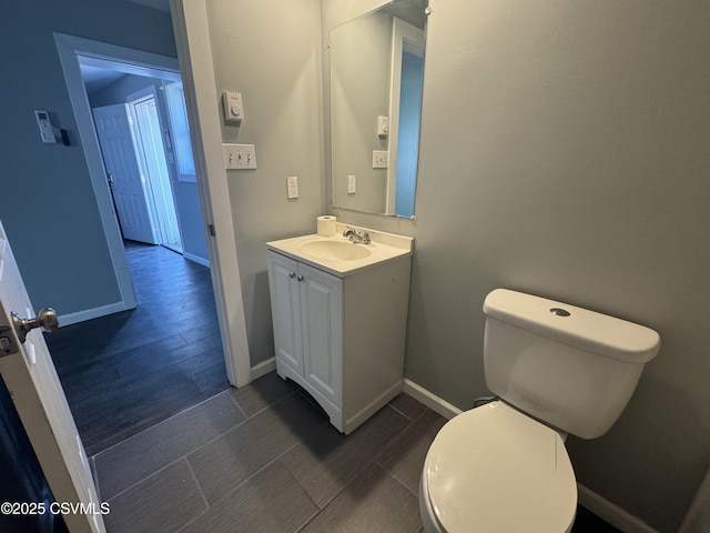 half bathroom featuring toilet, baseboards, wood finish floors, and vanity