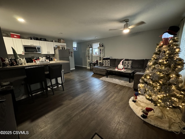 living area featuring a ceiling fan, dark wood finished floors, and baseboards