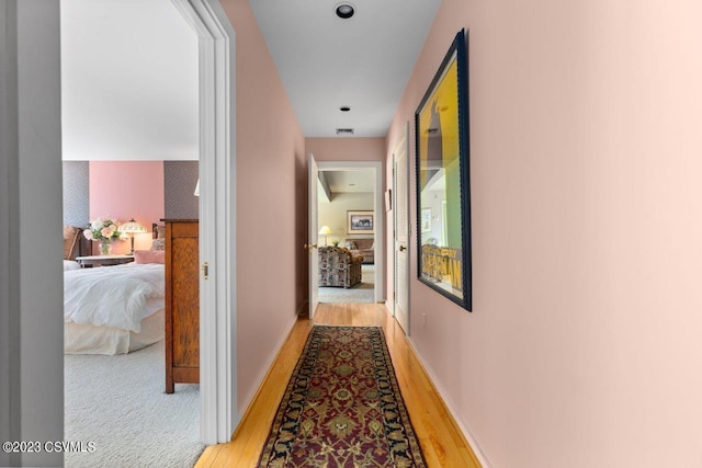 hall featuring light wood-type flooring, visible vents, and baseboards