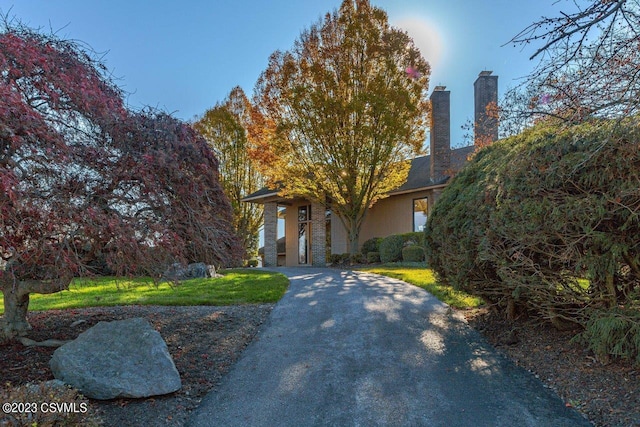 view of front facade featuring driveway, stucco siding, a chimney, and a front yard