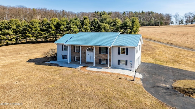 bi-level home with a porch, brick siding, a front yard, and metal roof