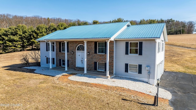 bi-level home with brick siding, metal roof, a front yard, and driveway