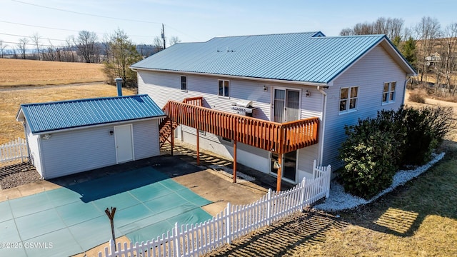 rear view of property with fence, a patio area, a wooden deck, metal roof, and an outbuilding