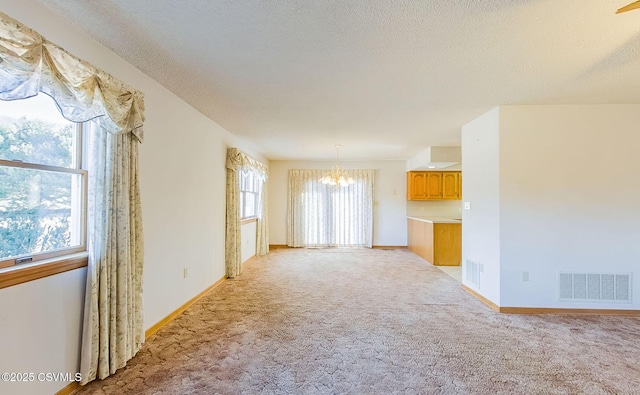 unfurnished living room featuring visible vents, light carpet, a textured ceiling, and an inviting chandelier