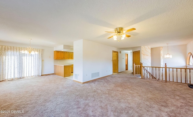 unfurnished living room with ceiling fan with notable chandelier, light colored carpet, visible vents, and a textured ceiling