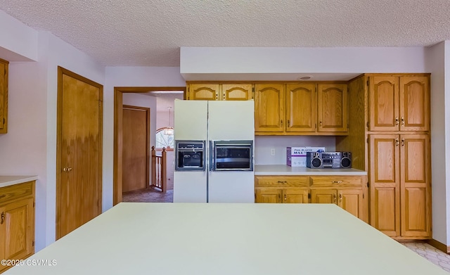 kitchen with brown cabinets, a textured ceiling, white refrigerator with ice dispenser, and light countertops