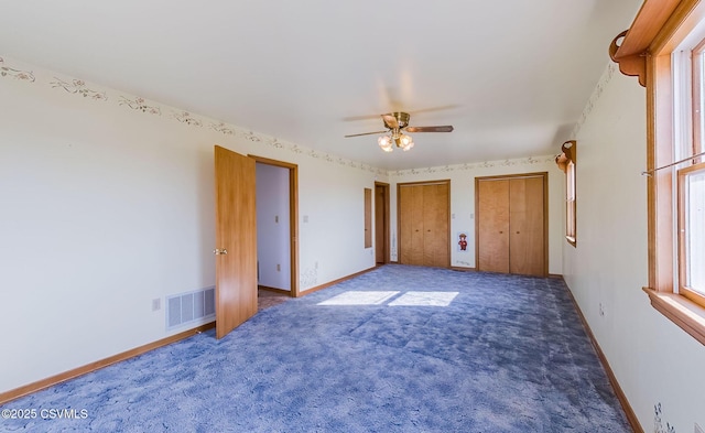 unfurnished bedroom with visible vents, carpet flooring, two closets, and baseboards