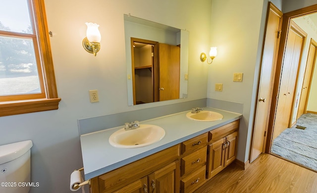 bathroom featuring double vanity, toilet, wood finished floors, and a sink